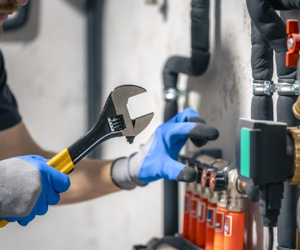 A man installs a heating system in a house and checks the pipes with a wrench. A man installs a heating system in a house and checks the pipes with a wrench. Adjusting heating valves in a residential building. A plumbing and heating technician works.
